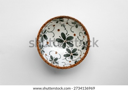 Overhead flat lay of decorative ceramic bowl with simple floral pattern and natural tones, isolated on white background, photographed using soft diffused lighting and clean composition.