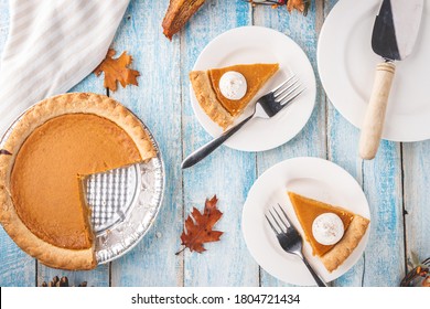 Overhead Flat Lay Shot Of A Pumpkin Pie In A Tin With Two Slices Of Pumpkin Pie On Plates With Forks On A Rustic Blue Painted Wooden Table Surface.