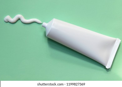 An overhead (flat lay) shot of a squiggly line of compounded, white cream being squeezed out of a prescription pharmacy ointment tube onto a light green background.  Room for text (copy).