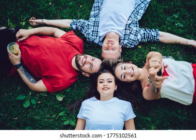 Overhead Flat Lay View Of Caucasian Group Of Cheerful Male And Female Hipsters Lying In Circle On Grass And Smiling At Camera During Time For Weekend Picnic In Park, Only Good Vibes Allowed