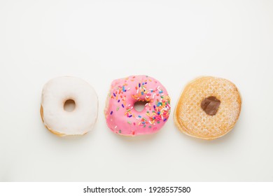 Overhead flat lay view of three fresh, colourful ring doughnuts in a row isolated on a plain white surface and background. - Powered by Shutterstock