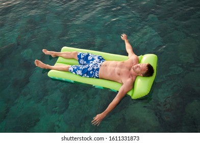 Overhead full length view of man relaxing on a green inflatable lilo floating on the water - Powered by Shutterstock