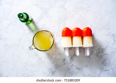 Overhead Of Ginger Simple Syrup For A Moscow Mule Popsicle With Ginger Ale And Popsicle Molds On A White Marble Surface.