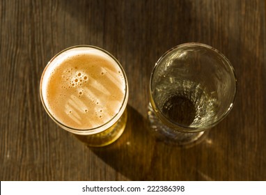 Overhead of Glass of Beer Beside Empty Glass on Wooden Table