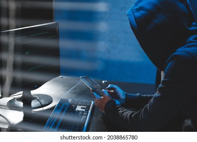 Overhead hacker in hood working at computer and mobile phone typing text in dark room, An anonymous hacker uses malware with mobile phone to hack password, personal data steals money from bank. cyber