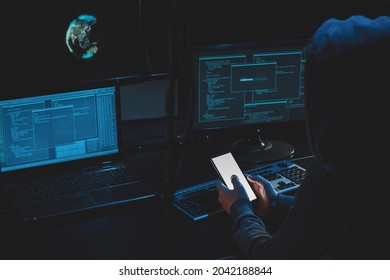Overhead hacker in hood working at laptop and mobile phone typing text in dark room, An anonymous hacker uses malware with mobile phone to hack password, personal data steals money from bank. cyber