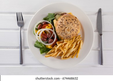 Overhead Of Hamburger, French Fries, And Salad In Plate On Wooden Table