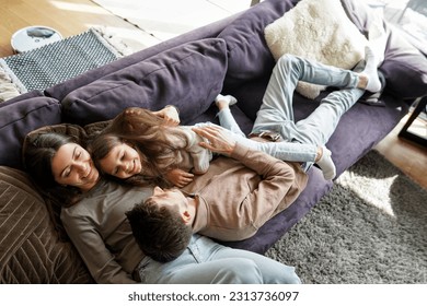Overhead high angle view on young parents and little daughter preschool girl child lying on sofa couch relaxing, hugging having fun day off time at home living room. Funny family activity on weekend