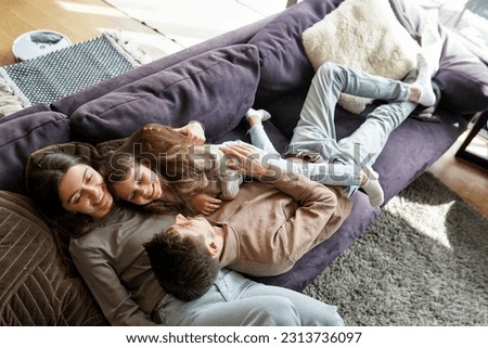 Overhead high angle view on young parents and little daughter preschool girl child lying on sofa couch relaxing, hugging having fun day off time at home living room. Funny family activity on weekend