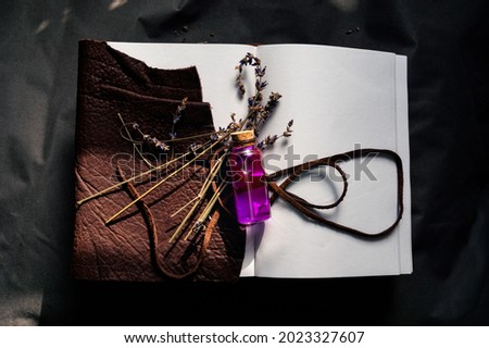 Overhead image of a glass stopper bottle with pink liquid and dried lavender on top of an open brown leather-bound notebook.