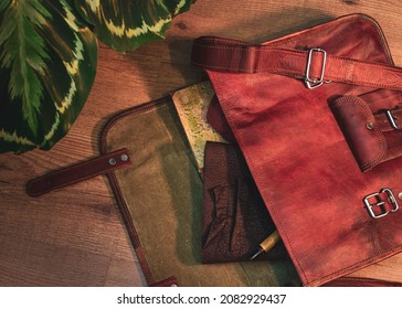 Overhead Image Of An Open Brown Leather Messenger Bag Containing A Book A Leather Notebook And A Pen