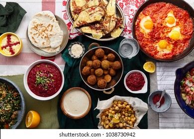 Overhead image of traditional jewish and middle eastern food: falafel, fattoush, tabouli, shakshuka, balila, hummus, roasted eggplants and spicy beetroot dip. Israeli cuisine concept