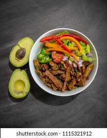 Overhead Image Of A Vegan Burrito Bowl, With Seitan As The Meat Substitute, Served Rice, Lettuce, Red And Yellow Bell Peppers, And A Sliced Avocado On The Side.