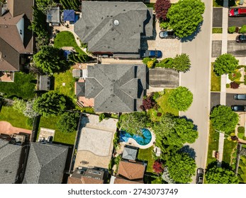Overhead looking down at a community of detached homes and properties lining a street with green trees, driveways, and parked cars, showcasing urban planning and growth