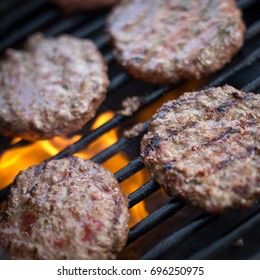 Overhead Macro Closeup Perspective Of Homemade Recipe Beef Hamburger Meat Patties Charred By Grill Marks And Lines Cooking On Black Charcoal Barbecue Grates And Flame Background At Backyard Cookout