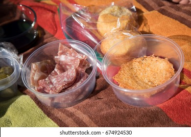 Overhead Outdoor Homemade Park Picnic Scene With Melted Cheese Crisp And Reusable Container With Finger Food Snacks Of Salami And Pickles With Corn Bread Muffin On Striped Colorful Table Cloth Blanket