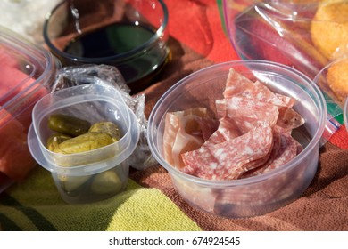 Overhead Outdoor Homemade Park Picnic Scene With Balsamic Vinegar And Reusable Container With Finger Food Snacks Of Salami And Pickles With Corn Bread Muffin On Striped Colorful Table Cloth Blanket