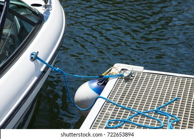 Overhead Perspective Close Up Of A Modern Motorboat Parked In A Boat Slip At A Waterfront Marina, With Blue Lashing Ropes Fender Buoy