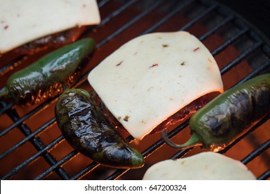 Overhead Perspective Of Organic Grass Fed Beef Burger Patty Covered In Slice Of Melting Pepper Jack Cheese Beside Blackened Spicy Green Jalapenos On Barbecue Grate With Glowing Red And Orange Charcoal