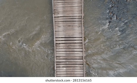 Overhead perspective of a rustic timber bridge crossing over murky flowing river water.