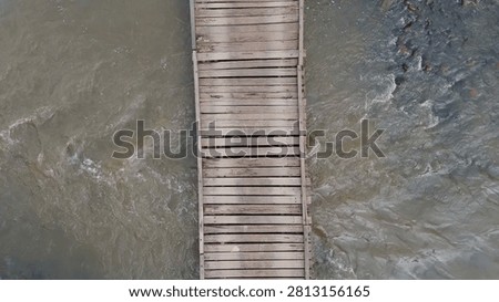 Overhead perspective of a rustic timber bridge crossing over murky flowing river water.