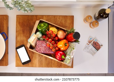 Overhead Of Phone With Recipe Cards By Box From Online Meal Food Recipe Kit Delivered To Home