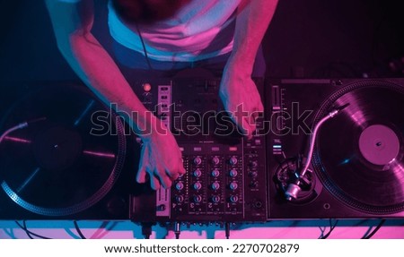 Overhead photo of disc jockey mixing records on party in night club. Professional hip hop DJ plays set on stage, focus on hands