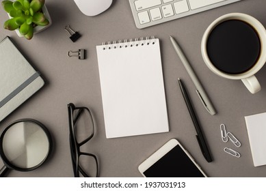 Overhead photo of empty notebook keyboard computer mouse magnifier pens phone plant glasses cup of coffee and paperclips isolated on the grey background