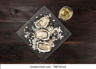 An Overhead Photo Of Freshly Opened Oysters On Ice, With A Glass Of White Wine And Copy Space, On Dark Textures