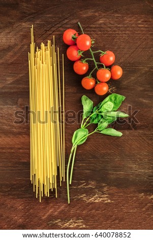 An overhead photo of a letter P for pasta, formed by spaghetti, cherry tomatoes, and a sprig of basil leaves, on a dark wooden background texture with copy space