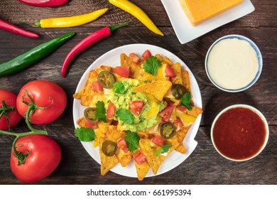 An Overhead Photo Of Nachos With Queso, Traditional Mexican Snack, With Ingredients Like Tomatoes, Chilli Peppers, Cheddar Cheese, And White And Red Sauces