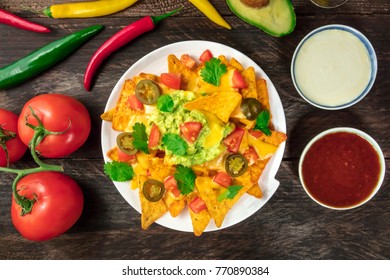 An Overhead Photo Of Nachos With Queso, Traditional Mexican Snack, With Ingredients Like Tomatoes, Chilli Peppers, Avocado, And White And Red Sauces