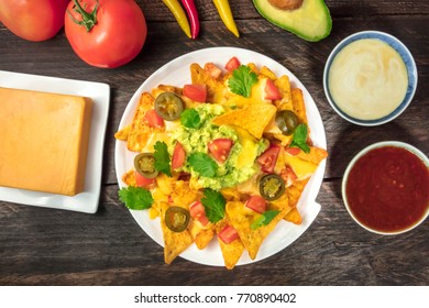 An Overhead Photo Of Nachos With Queso, Traditional Mexican Snack, With Ingredients Like Tomatoes, Chilli Peppers, Cheddar Cheese, Avocado, And White And Red Sauces