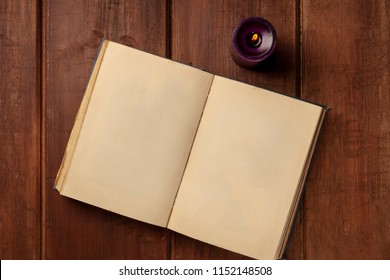 An overhead photo of an old book with a burning candle, shot from above on a dark rustic background