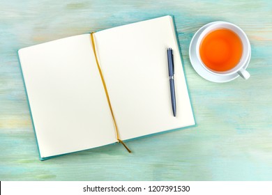 An overhead photo of an open journal notebook with a pen and a cup of tea, shot from above, a diary on a teal blue background with a place for text