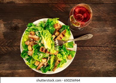 An Overhead Photo Of A Plate Of Chicken Caesar Salad With A Fork And A Glass Of Rose Wine, On A Dark Rustic Background With A Place For Text