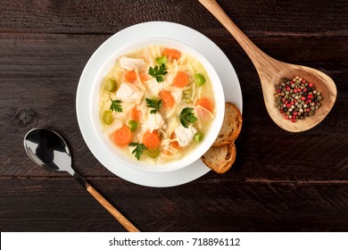 An Overhead Photo Of A Plate Of Chicken And Noodles Soup, Shot From Above On A Dark Rustic Texture With A Spoon, A Wooden Ladle With Peppercorns, Slices Of Bread, And A Place For Text