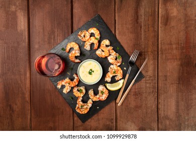 An Overhead Photo Of Plate Of Cooked Shrimps On A Dark Rustic Background, With A Sauce And A Glass Of Wine, With Copy Space