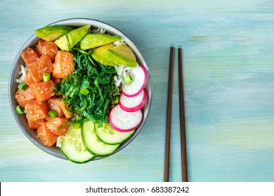An overhead photo of poke, traditional Hawaiian raw fish salad, with chopsticks and copy space, on a teal blue background texture - Shutterstock ID 683387242