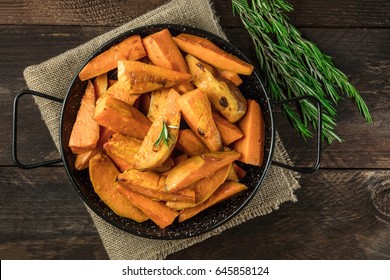 An Overhead Photo Of Roasted Sweet Potatoes In A Pan, Shot From Above On Dark Rustic Wooden Textures With Rosemary Branches, With A Place For Text