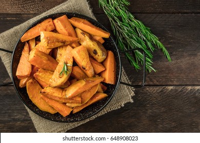 An Overhead Photo Of Roasted Sweet Potatoes In A Pan, Shot From Above On Dark Rustic Wooden Textures With Rosemary Branches.