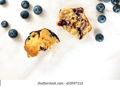 An Overhead Photo Of Two Halves Of A Blueberry Muffin With Fresh Blueberries Scattered Around, With A Place For Text