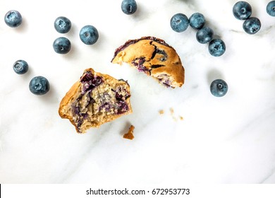 An Overhead Photo Of Two Halves Of A Blueberry Muffin With Fresh Blueberries And Crumbs Scattered Around, With A Place For Text