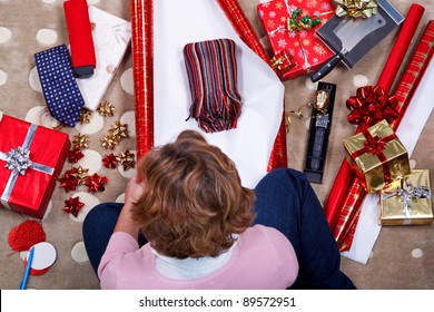 Overhead photo of a woman sat on a rug at home wrapping her Christmas presents surrounded by gifts, paper, ribbon and bows. - Powered by Shutterstock