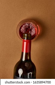 Overhead Photography Of A Bottle Of Red Wine Pouring Into A Stemless Wine Glass Against A Warm Caramel Coloured Background