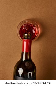 Overhead Photography Of A Bottle Of Red Wine Pouring Into A Stemless Wine Glass Against A Warm Caramel Coloured Background