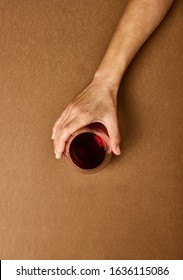 Overhead Photography Of A Light Skin Woman's Hand Holding A Stemless Wine Glass Against A Warm Caramel Coloured Background