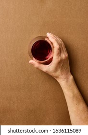 Overhead Photography Of A Light Skin Woman's Hand Holding A Stemless Wine Glass Against A Warm Caramel Coloured Background