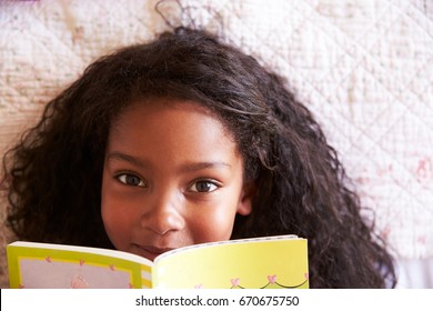 Overhead Portrait Of Girl Lying On Bed And Reading Book
