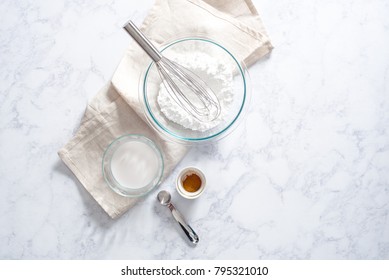 Overhead Of Powdered Sugar In Glass Bowl With Wire Whisk And Cream, Cinnamon And Silver Tablespoon.